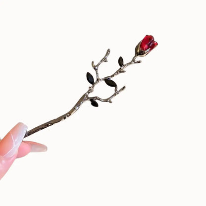 Épingle à tige sombre surmontée d’une rose rouge.