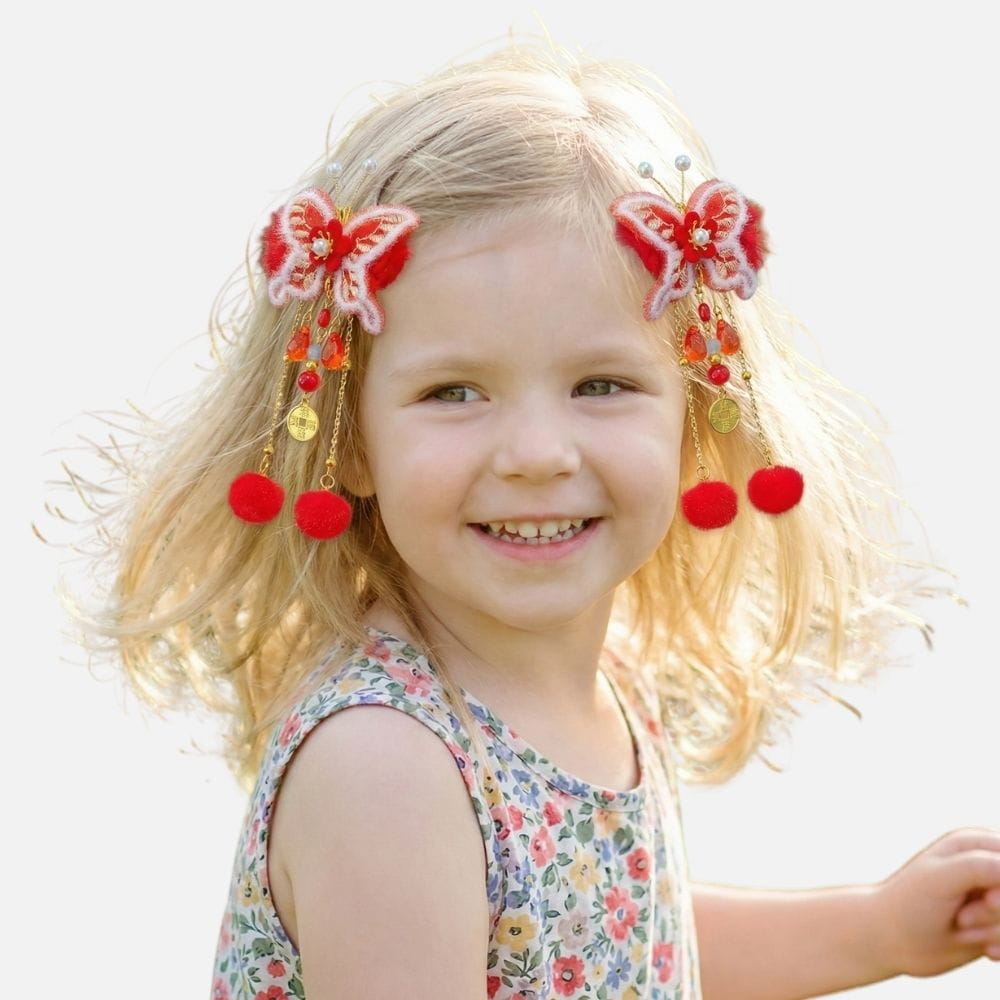 Une petite fille souriante porte des accessoires colorés en forme de papillon et des pompons rouges dans les cheveux