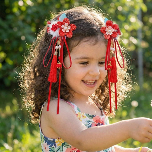 Une petite fille souriante porte des accessoires floraux rouges dans ses cheveux, entourée de verdure