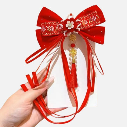 Un grand nœud rouge orné de fleurs et de perles, avec des rubans et une frange décorative