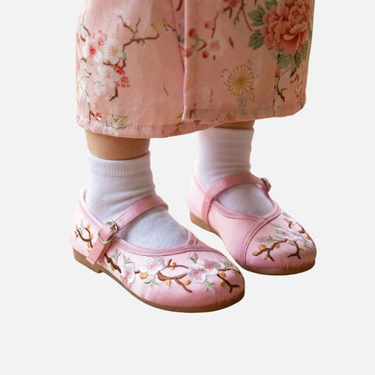Petits pieds d'enfant portant des ballerines roses ornées de fleurs sur un fond de jupe rose à motifs floraux