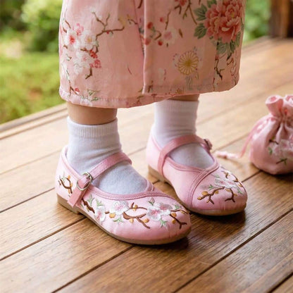 Petits pieds d'enfant dans des ballerines roses ornées de fleurs, sur un sol en bois naturel