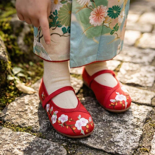 Des ballerines rouges ornées de fleurs, portées avec des chaussettes claires, sur un chemin en pierre