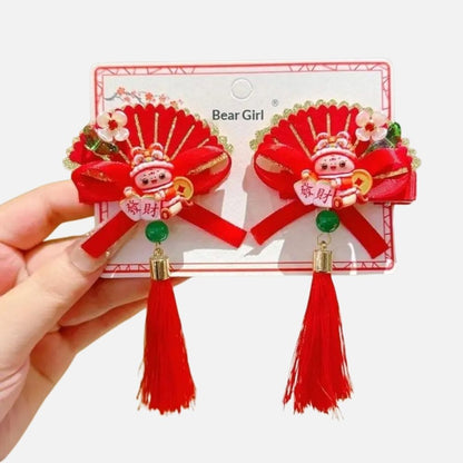 Deux broches décoratives rouges avec des motifs dorés, un personnage en céramique et des pompons en franges