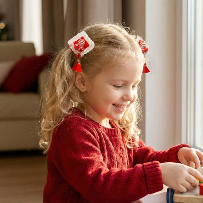 Une petite fille souriante porte un pull rouge et des barrettes décoratives, jouant près d'une fenêtre lumineuse
