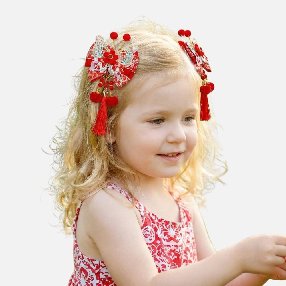 Une petite fille aux cheveux bouclés porte un haut rouge à motifs floraux et des accessoires de cheveux colorés