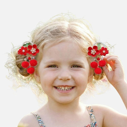 Une petite fille souriante avec des fleurs rouges dans les cheveux, portant une robe colorée, se tient dans un décor