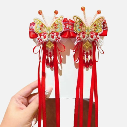 Deux ornements en forme de papillon, rouges et dorés, avec des rubans et des perles suspendus