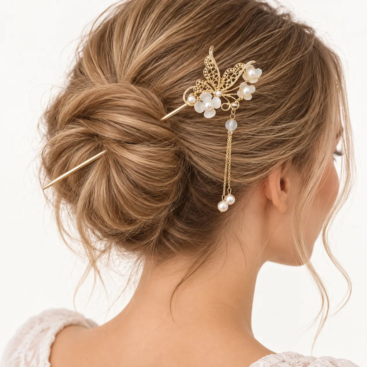 Chignon blond orné d’un bijou doré à feuillage et perles nacrées.