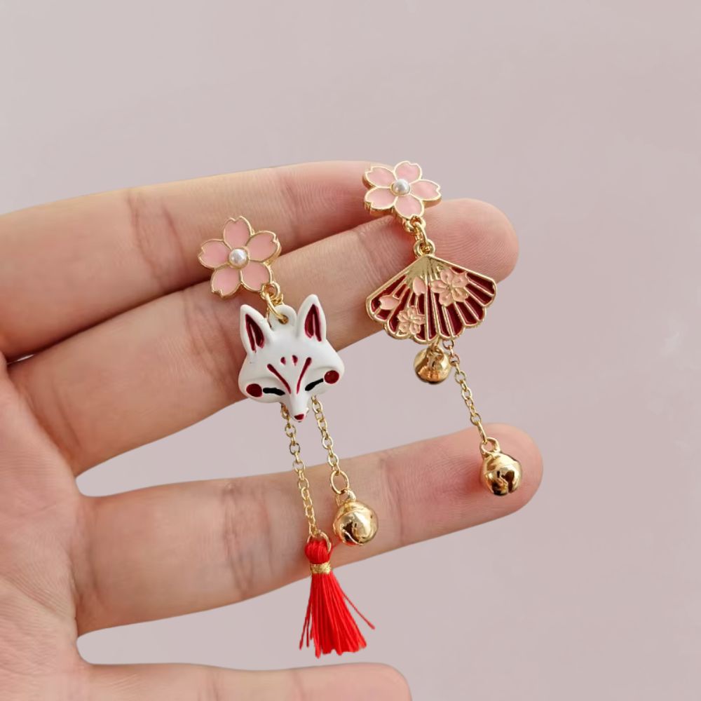 Boucles d'oreilles en métal doré avec un motif de renard blanc et des fleurs roses, évoquant un style japonais.