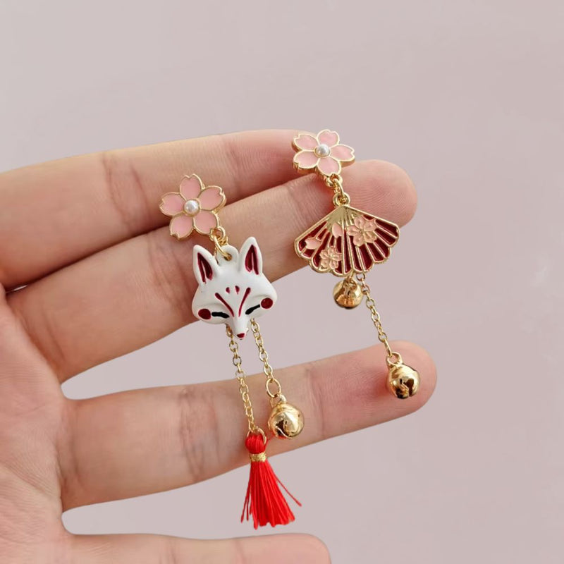 Boucles d'oreilles en métal doré avec un motif de renard blanc et des fleurs roses, évoquant un style japonais.