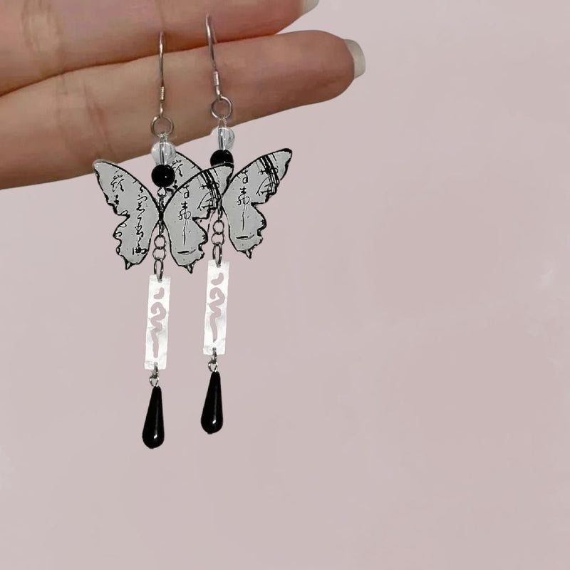 Boucles d'oreilles en forme de papillon avec motifs de calligraphie japonaise, noir et argenté, suspendues à une main