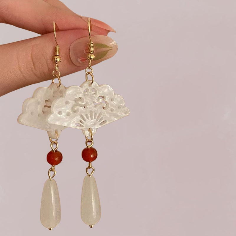 Boucles d'oreilles en forme d'éventail, ornées de perles rouge et blanche, suspendues par des crochets dorés, évoquant un style japonais.