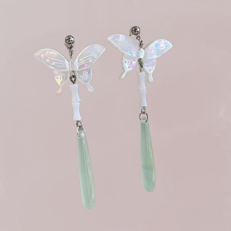 Boucles d'oreilles en forme de papillon, nacrées et légères, avec des pendants en jade vert, sur fond rose.