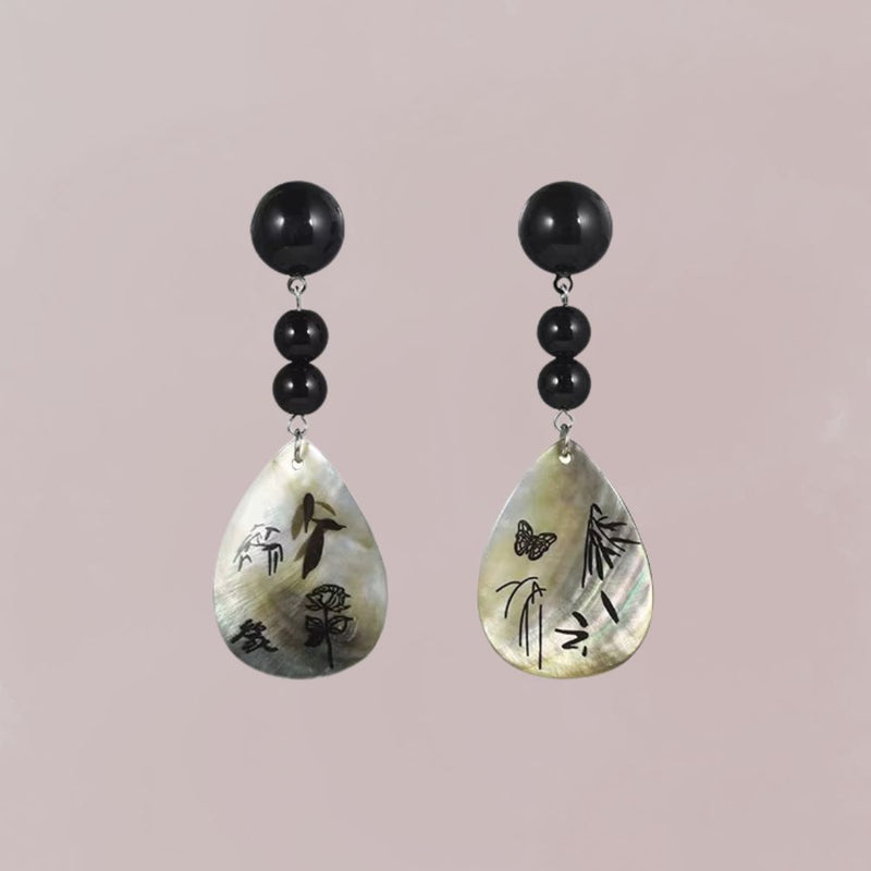 Boucles d'oreilles en nacre avec motifs poétiques, perles noires et forme goutte, évoquant un style japonais élégant.