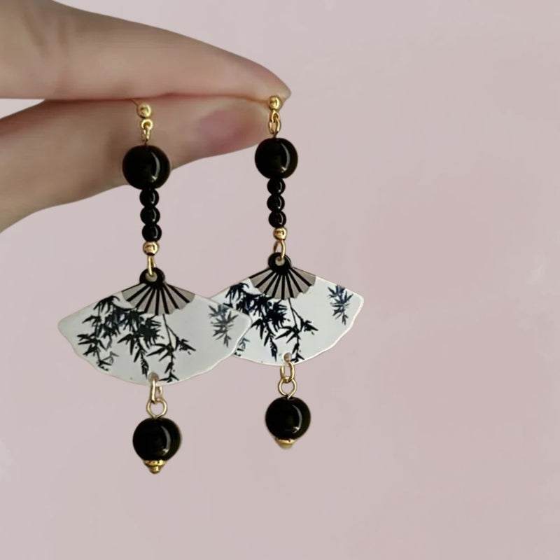 Boucles d'oreilles en forme d'éventail, avec motifs de bambou sur fond blanc et perles noires, évoquant le style japonais.