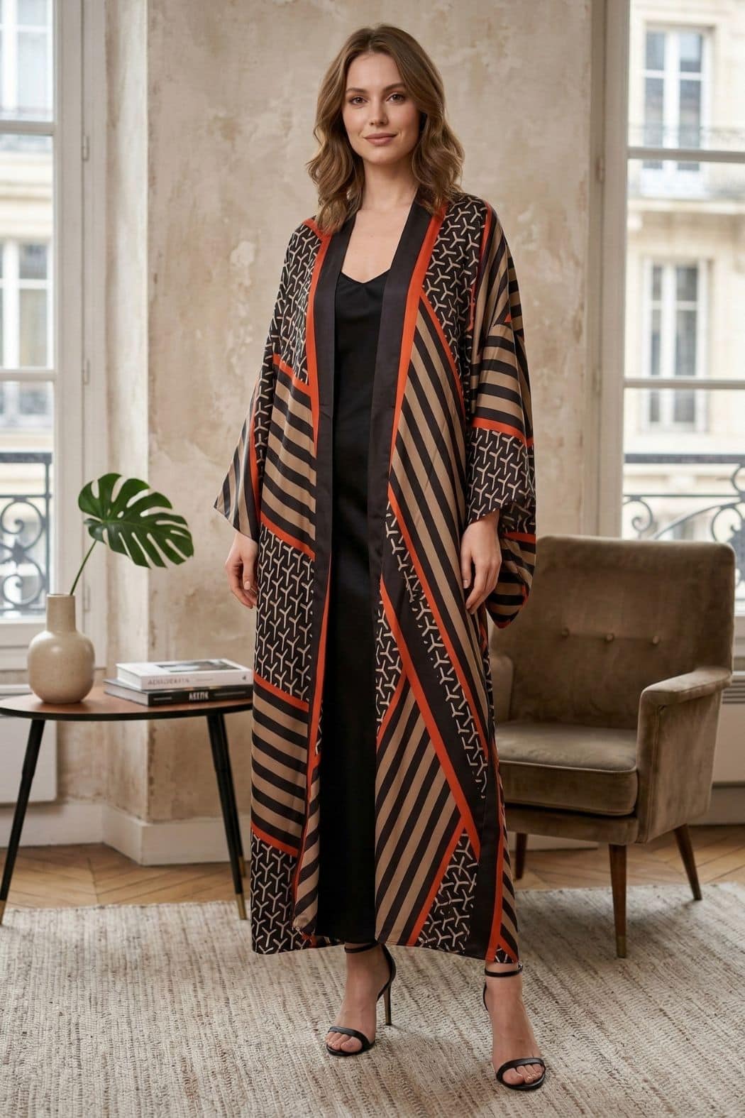 Femme portant un cardigan kimono aux motifs géométriques noirs, bruns et rouges, dans un décor élégant et lumineux