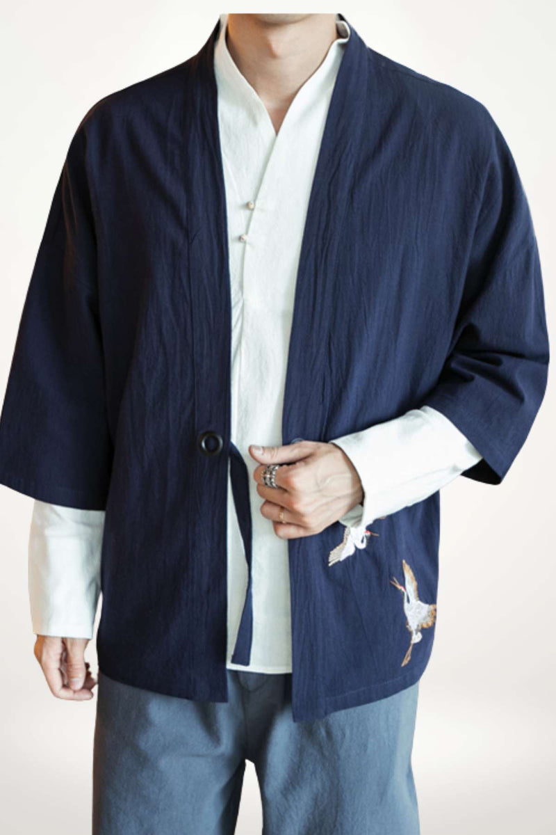 Homme portant une chemise kimono bleu marine avec des motifs de grues sur un fond clair