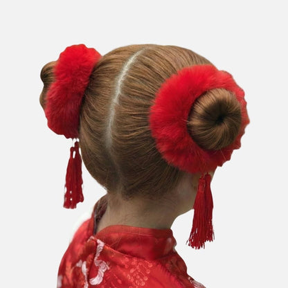 Coiffure traditionnelle avec deux chignons bruns ornés de pompons rouges et de franges, sur fond blanc