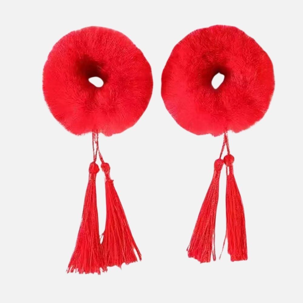Deux pompons rouges en textile doux avec des franges, suspendus par un cordon, sur fond blanc