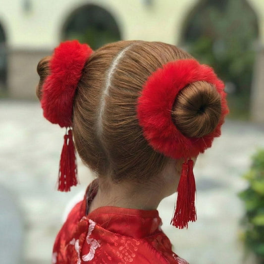 Coiffure en chignons avec accessoires rouges en fourrure, vêtue d'un kimono rouge, arrière-plan flou de jardin