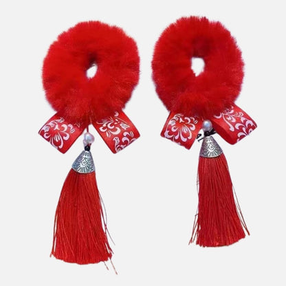 Deux ornements rouges en fourrure avec des rubans décoratifs et des franges, sur fond blanc