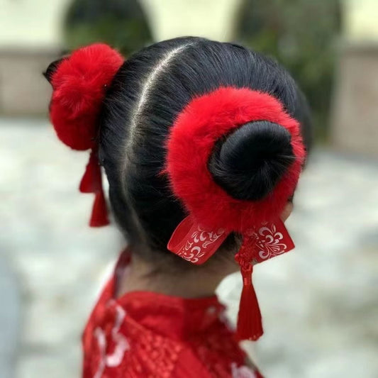 Coiffure traditionnelle avec un chignon noir, ornée de pompons rouges et de rubans, sur fond flou