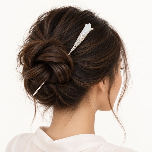 Chignon retenu par une épingle à fleur blanche sculptée.