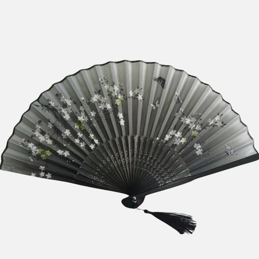 Éventail en tissu noir avec motifs de fleurs blanches et papillons, décoré d'un pompon noir