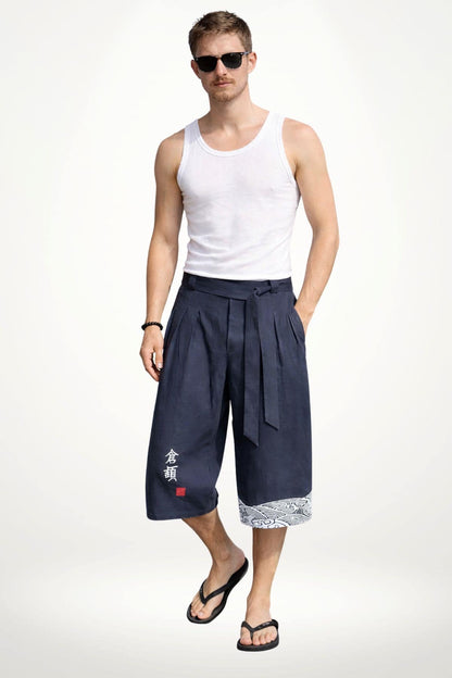 Homme portant un pantalon kimono bleu foncé, décoré de motifs blancs, dans une posture décontractée sur fond neutre