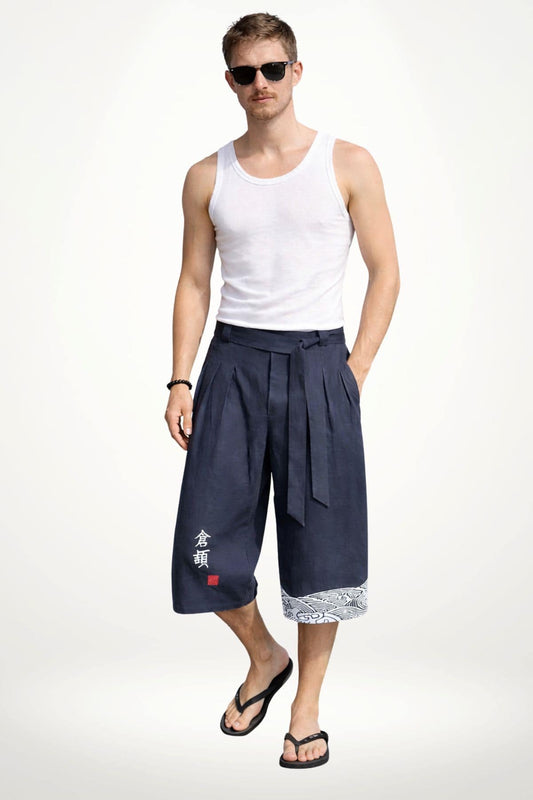 Homme portant un pantalon kimono bleu foncé, décoré de motifs blancs, dans une posture décontractée sur fond neutre