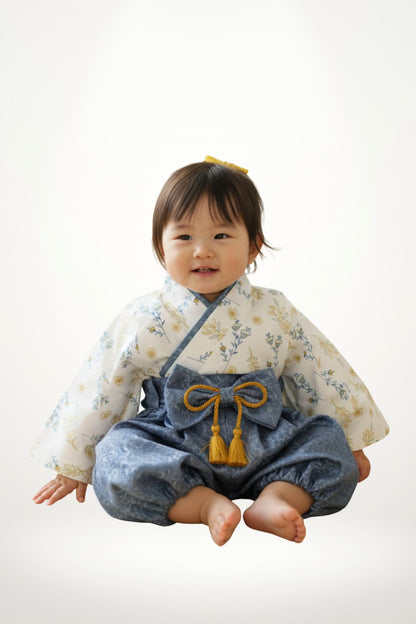 Bébé fille souriante en haori bleu gris avec motifs floraux, assise sur un fond neutre