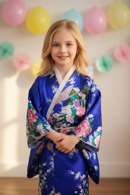 Une fille souriante porte un kimono bleu vif orné de fleurs roses et de motifs traditionnels, avec des manches larges