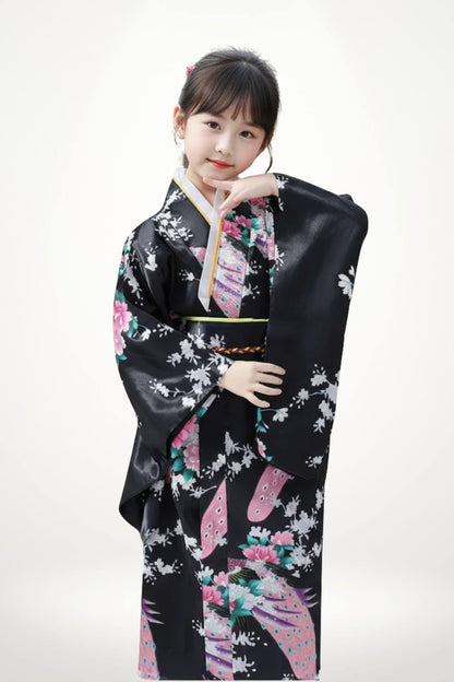 Fille en kimono noir orné de fleurs roses et blanches, posant avec élégance sur fond clair