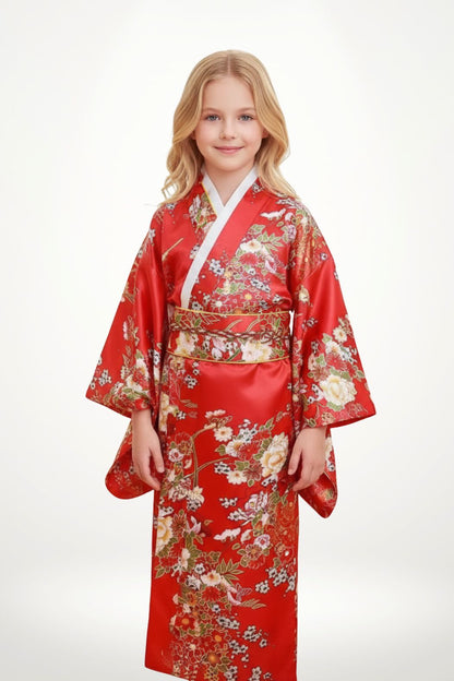 Une fillette souriante porte un kimono rouge orné de motifs floraux colorés sur un fond neutre