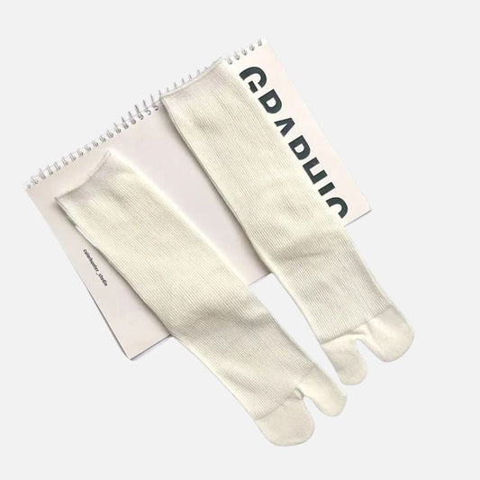 Chaussettes tabi blanches en matière côtelée, posées sur un carnet au design minimaliste