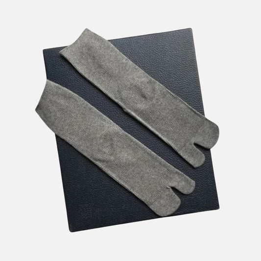 Chaussettes tabi grises posées sur un fond noir, avec une texture douce et un design élégant