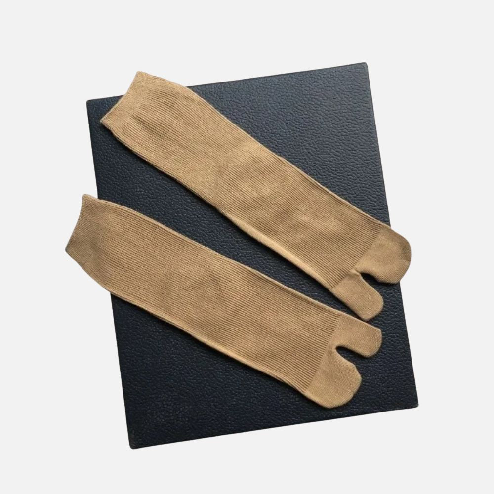 Chaussettes tabi camel en matière douce, posées sur un fond noir, avec une texture côtelée et une coupe unique