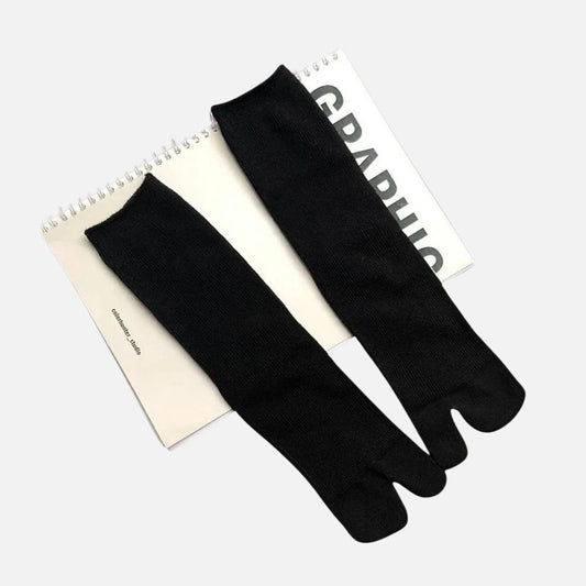 Chaussettes tabi noires en tricot, posées sur un carnet avec une couverture blanche et des lettres noires
