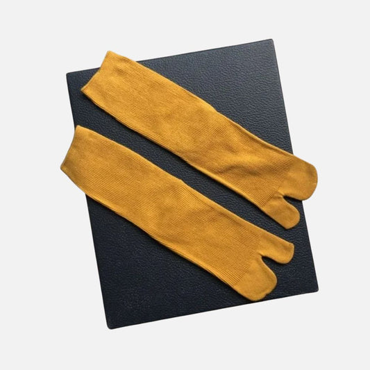 Chaussettes tabi en jaune ocre, avec une texture côtelée, posées sur un fond noir élégant