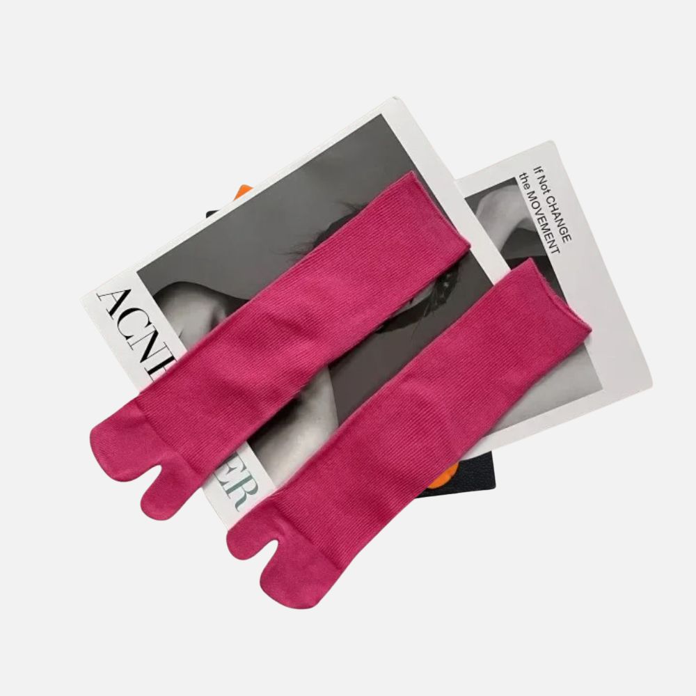 Chaussettes tabi fuchsia posées sur des magazines, avec une texture douce et un design élégant