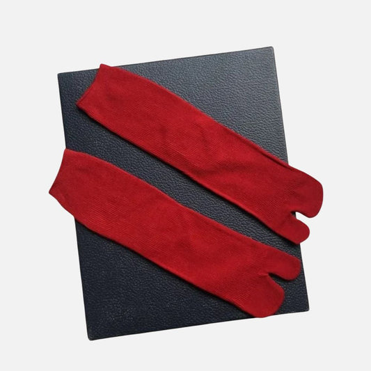 Chaussettes tabi rouges en tissu doux, posées sur un fond noir texturé, avec une coupe traditionnelle