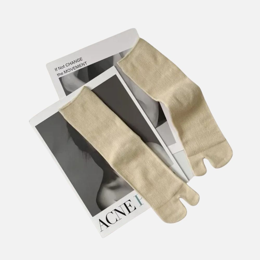 Chaussettes tabi beige posées sur des magazines en noir et blanc, avec une texture douce et un style épuré