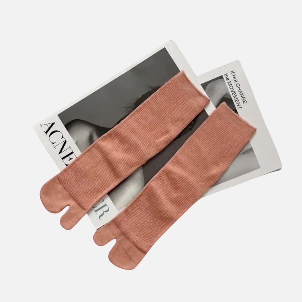 Chaussettes tabi rose poudre en matière douce, posées sur un magazine au fond neutre, créant une ambiance élégante