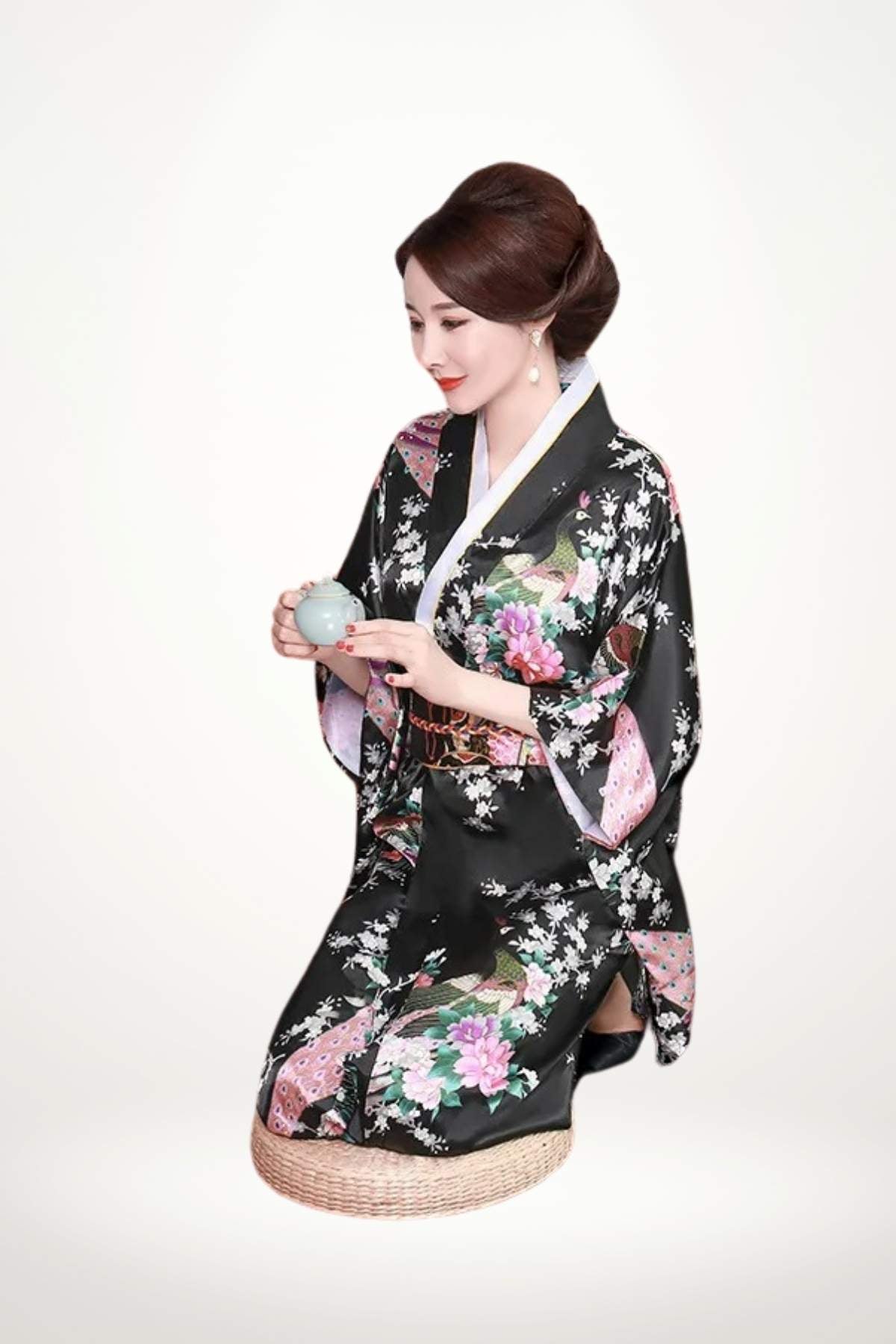 Femme assise en kimono noir à motifs floraux colorés, tenant une tasse, sur un fond neutre