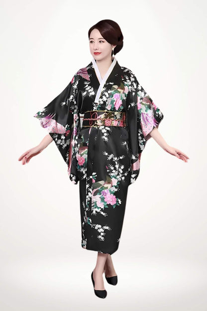 Femme en kimono noir à motifs floraux colorés, posant avec élégance sur fond clair