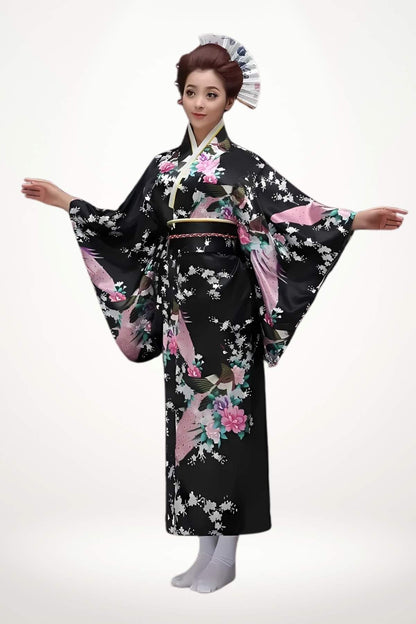 Femme debout en kimono long noir en satin à motifs floraux colorés et plumes exotiques, ceinture tressée inspirée du kimono traditionnelle.
