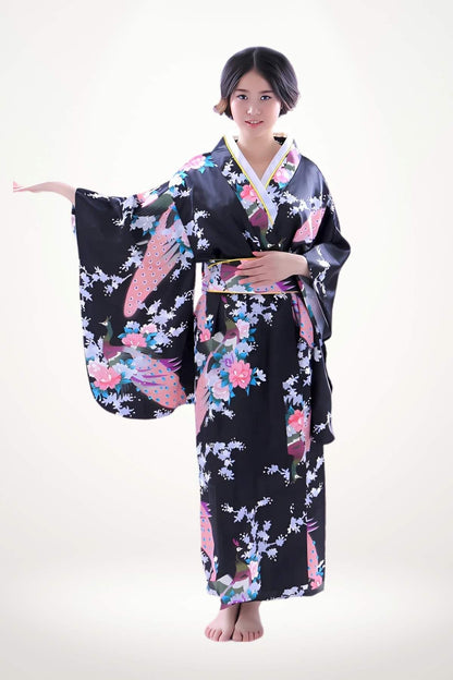Femme en kimono noir à motifs floraux colorés, posant avec élégance sur un fond clair