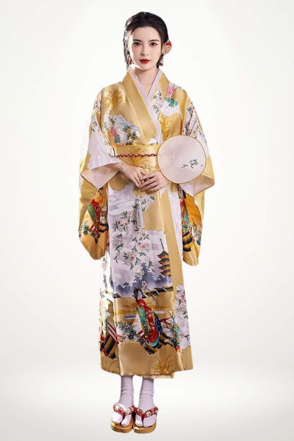 Femme en kimono doré à motifs floraux et scènes japonaises, posant avec un éventail dans un décor neutre