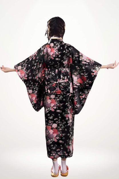 Femme en kimono noir à motifs floraux roses, bras étendus, sur fond clair, avec des sandales traditionnelles
